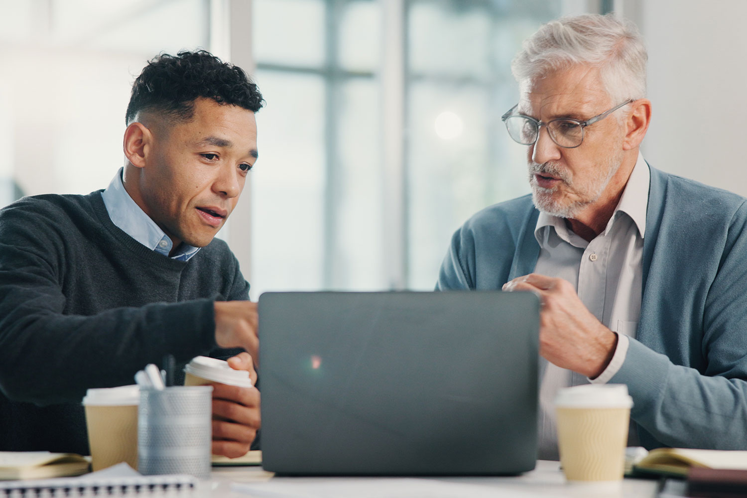 an accountant and a elderly client sat looking at a laptop with coffees on the table