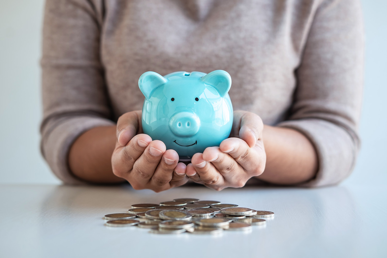 Woman holding a blue piggybank with coins spread out across the table
