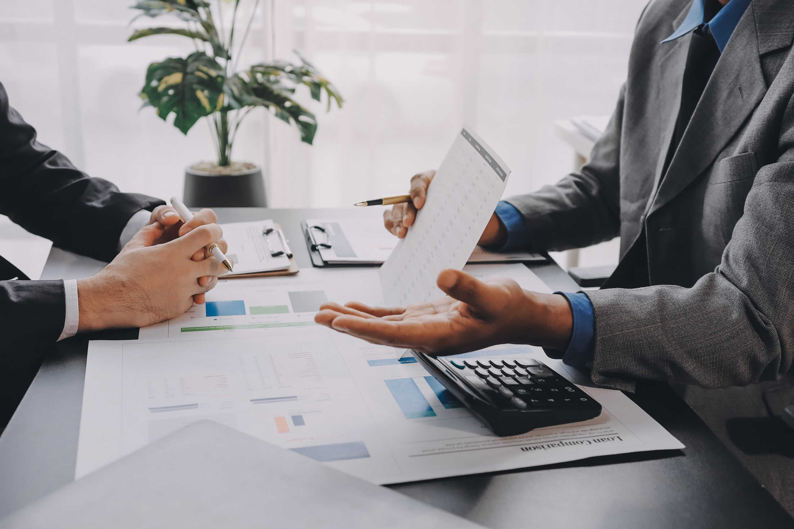 Shot of a table with a man in a suit holding up a graph appearing to explain it to another man in a suit who sits across from him.